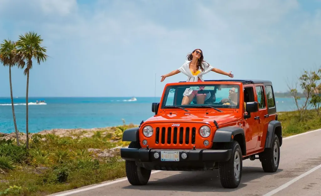 Guest standing out of an orange Jeep by the Caribbean